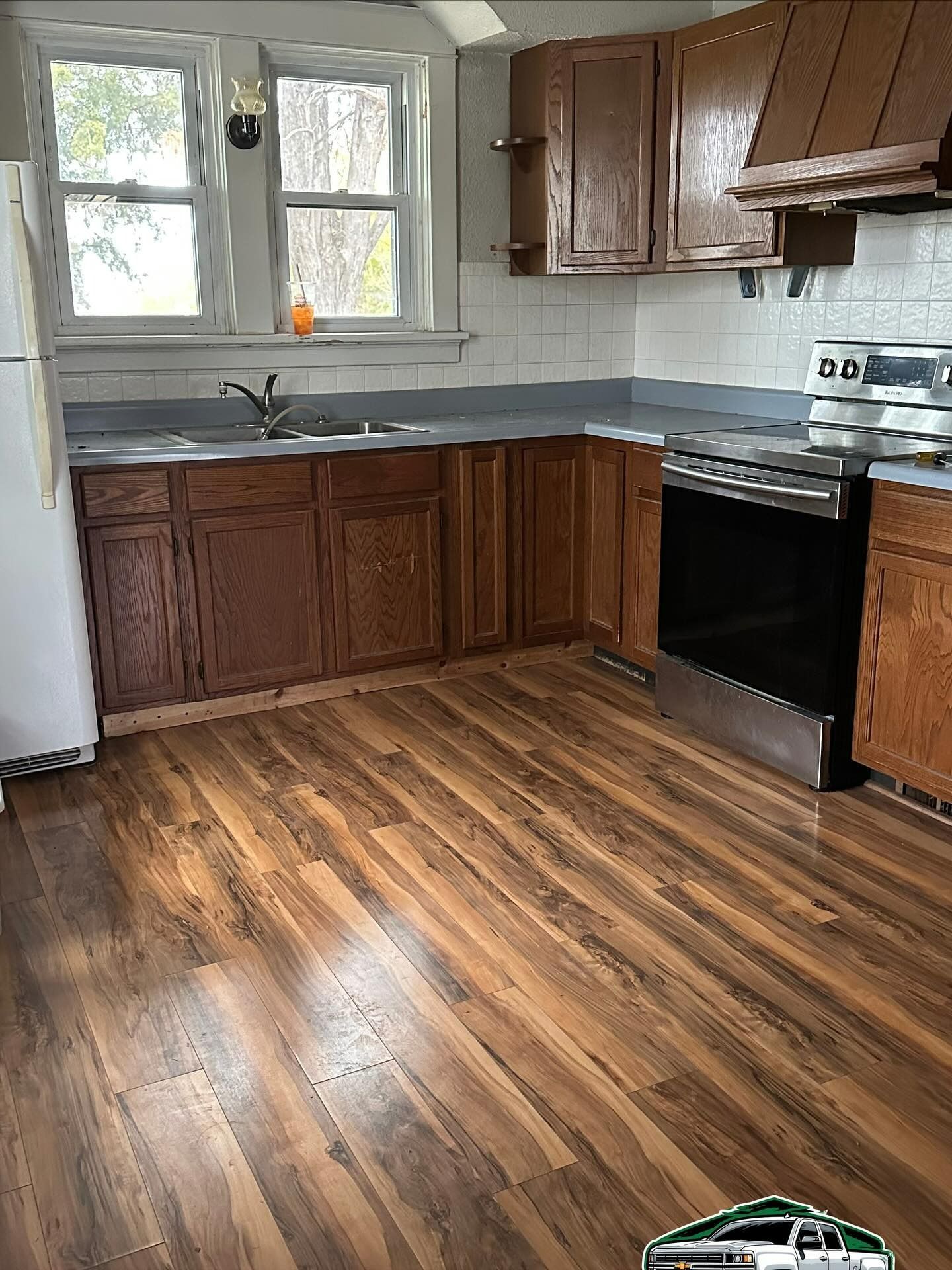 Kitchen with wooden cabinets, a stove, and wood-look flooring. Light from a window illuminates the space.