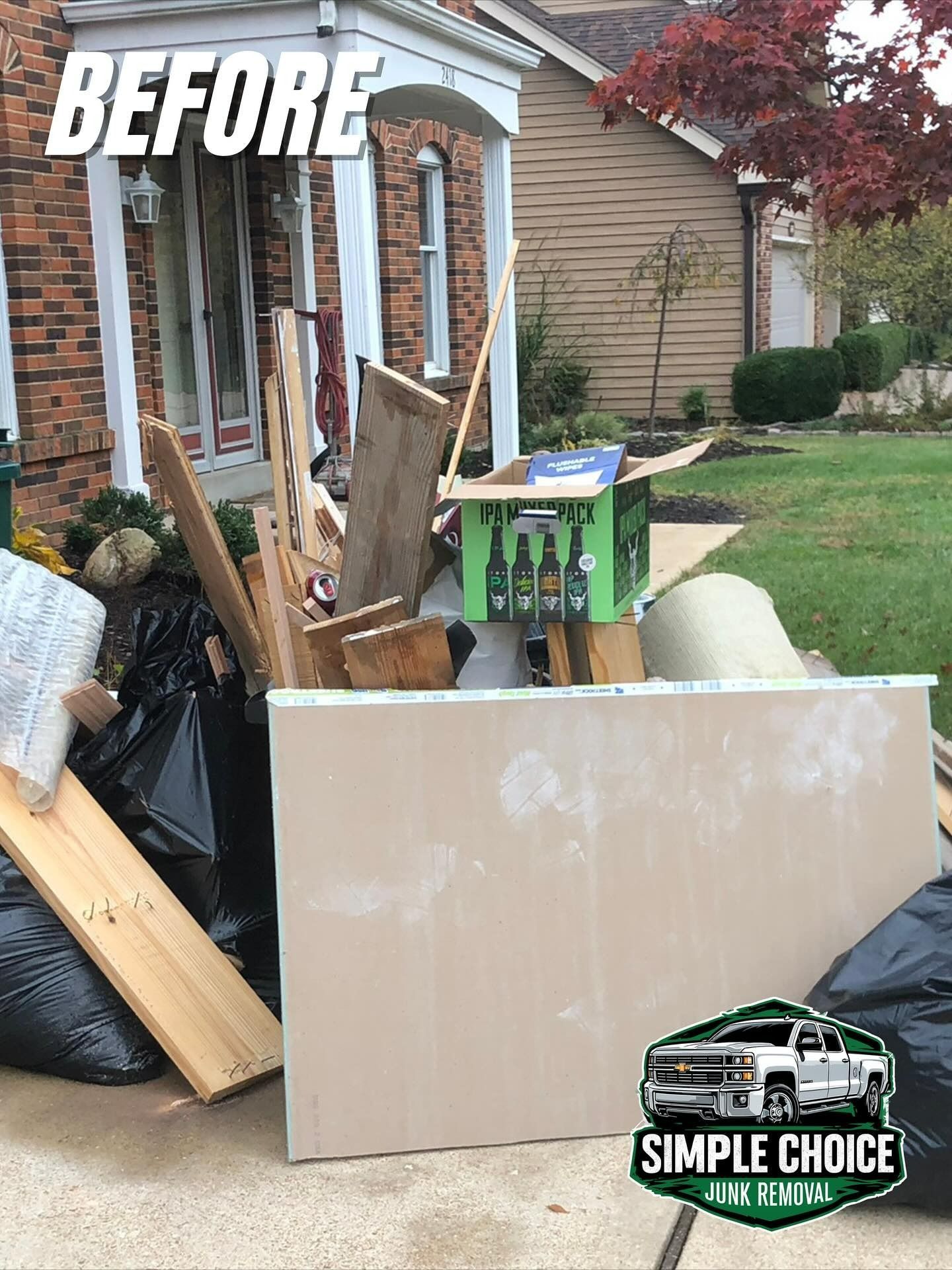Pile of debris on a driveway in front of a house, including wood, drywall, and trash bags. 
