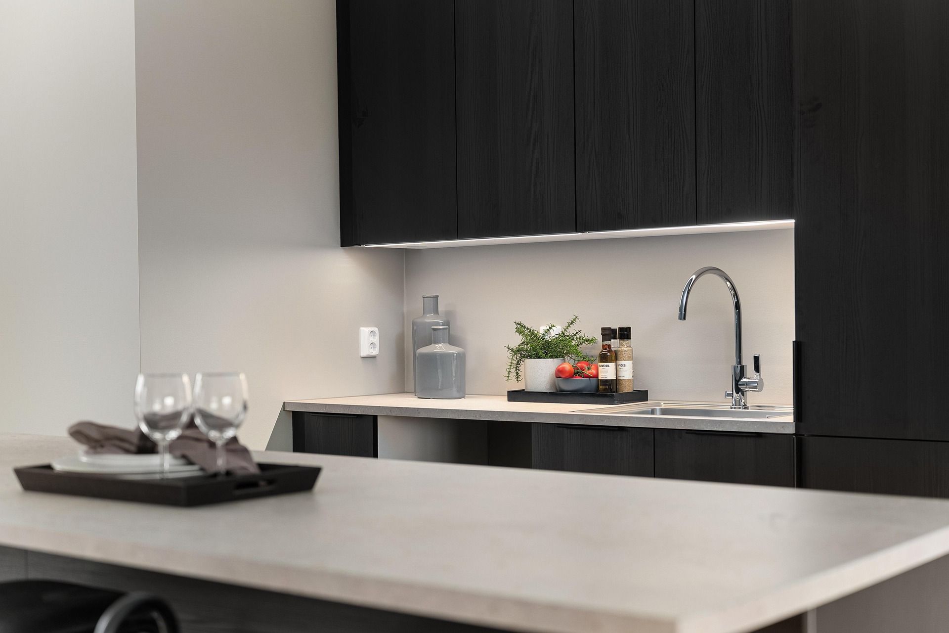 Cucina moderna con mobili in legno scuro, piano di lavoro chiaro, illuminazione sottopensile e vassoio di servizio.