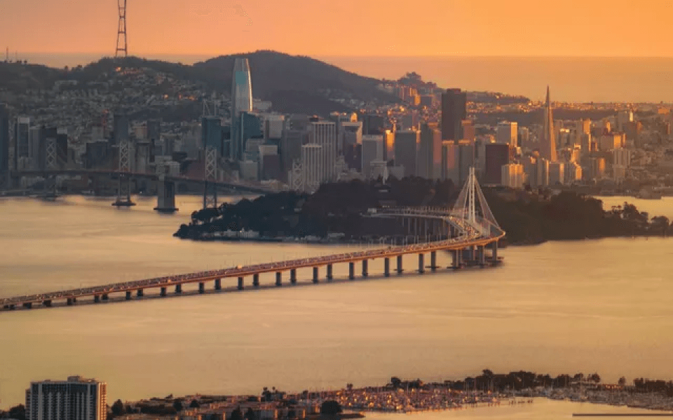 An aerial view of a bridge over a body of water with a city in the background.