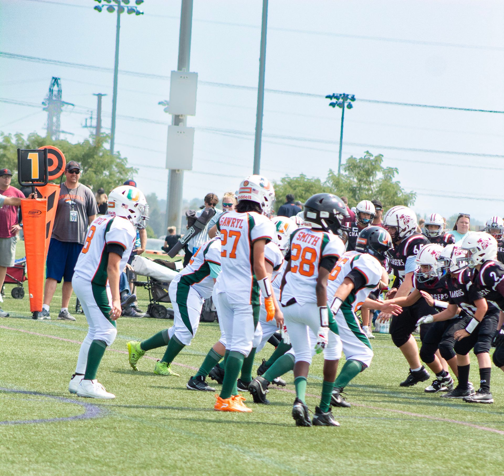 Football players in action on a grassy field; one runs with the ball, pursued by two opponents.