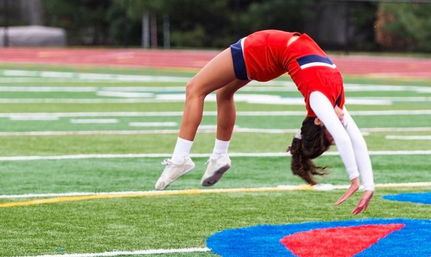 Cheerleader in red uniform performs a backbend on a green and red football field.