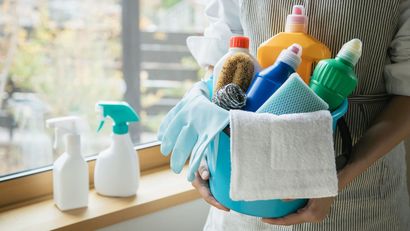 A woman is holding a blue bucket filled with cleaning supplies.