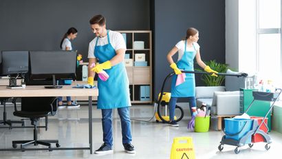 A man and a woman are cleaning an office with a vacuum cleaner.