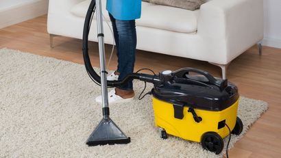 A woman is using a vacuum cleaner to clean a rug in a living room.