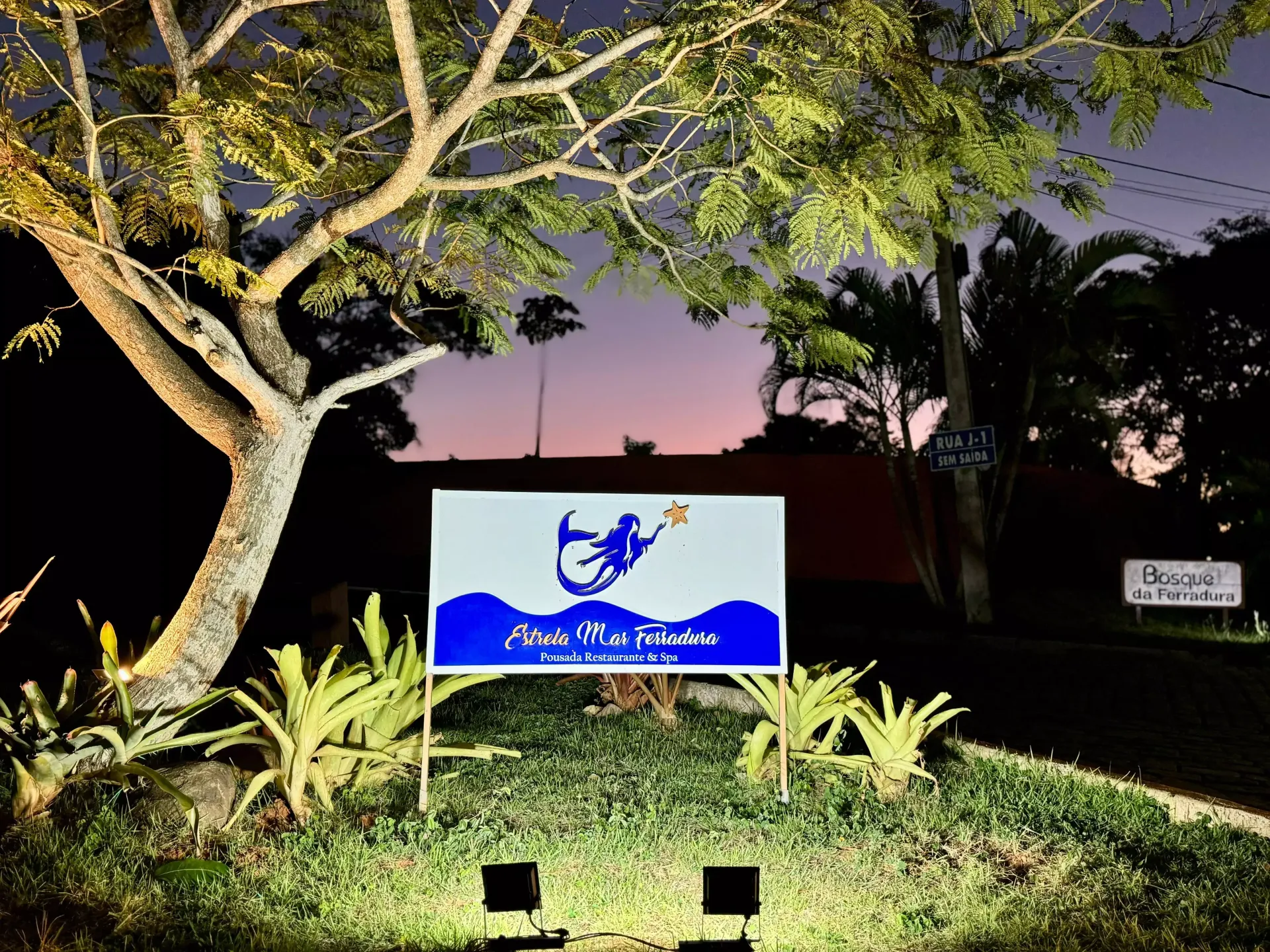 Uma placa azul com uma sereia é iluminada à noite - Pousada Estrelamar Ferradura