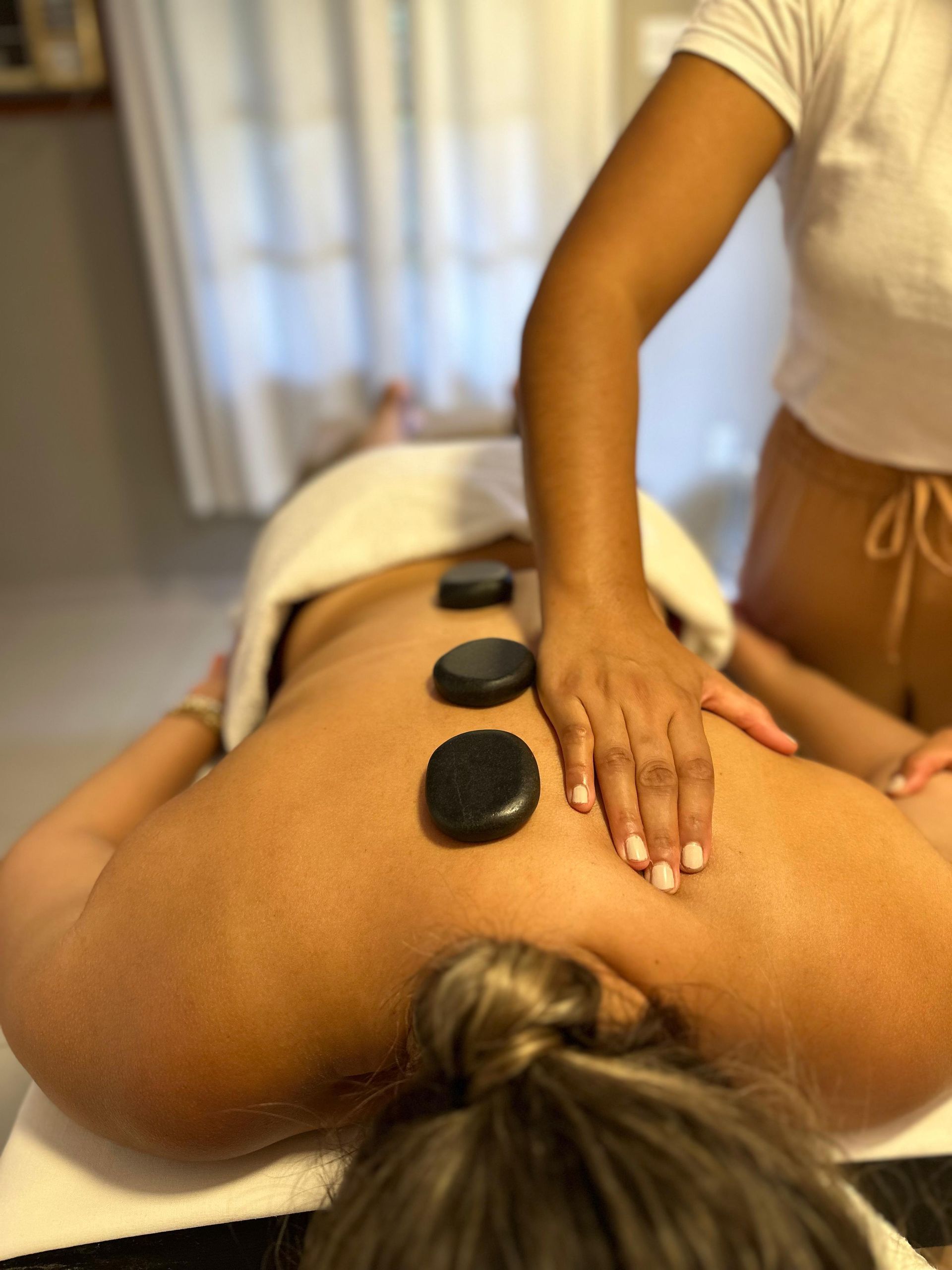 Uma mulher está recebendo uma massagem com pedras nas costas - Pousada-Estrelamar-Ferradura