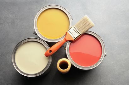 Four cans of paint and a brush on a table.