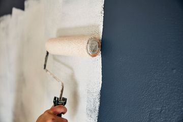 A person is painting a wall with a paint roller.