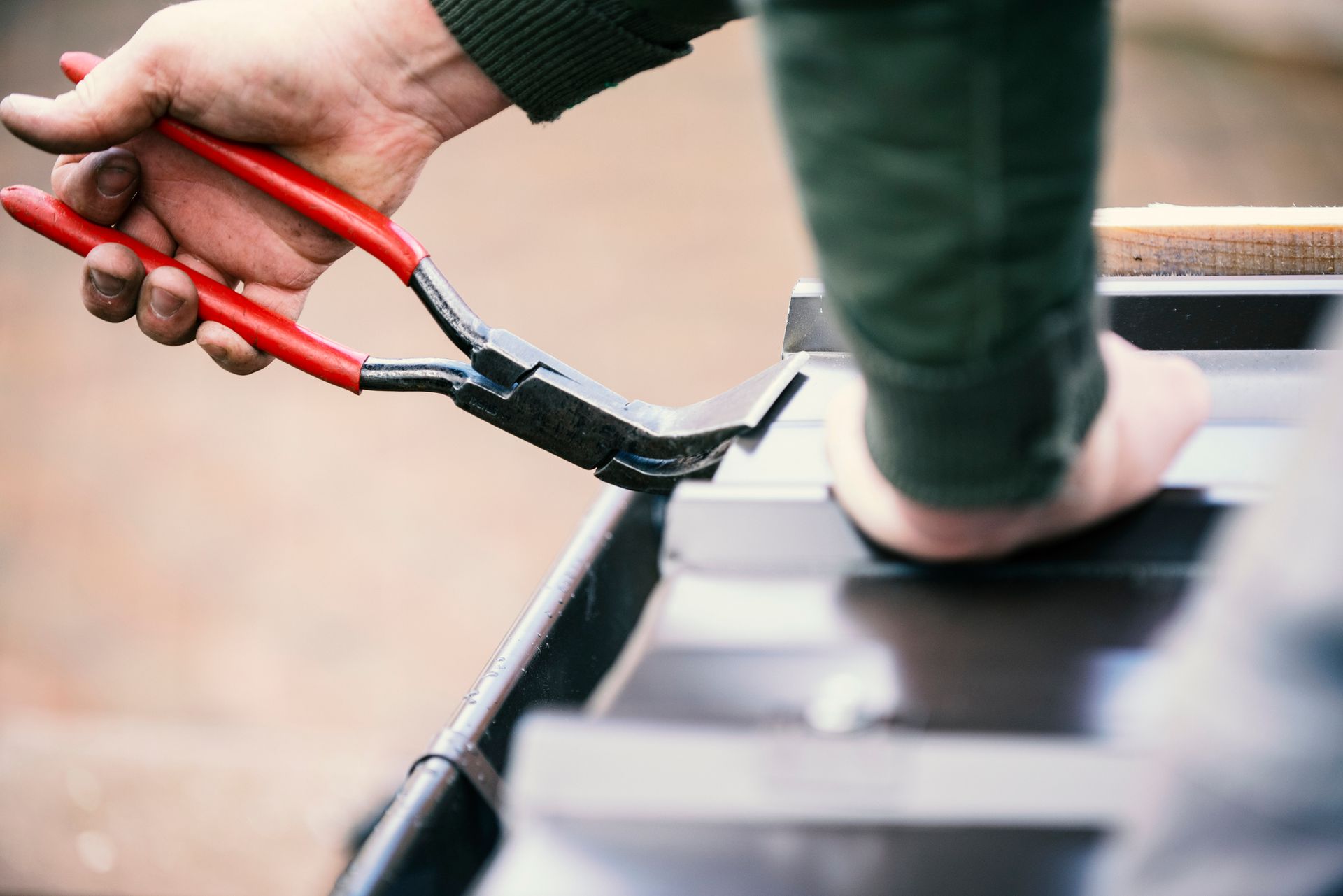 A person is holding a pair of pliers over a piece of metal.