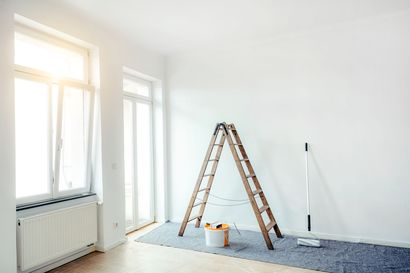 An empty room with a ladder , bucket of paint and mop.