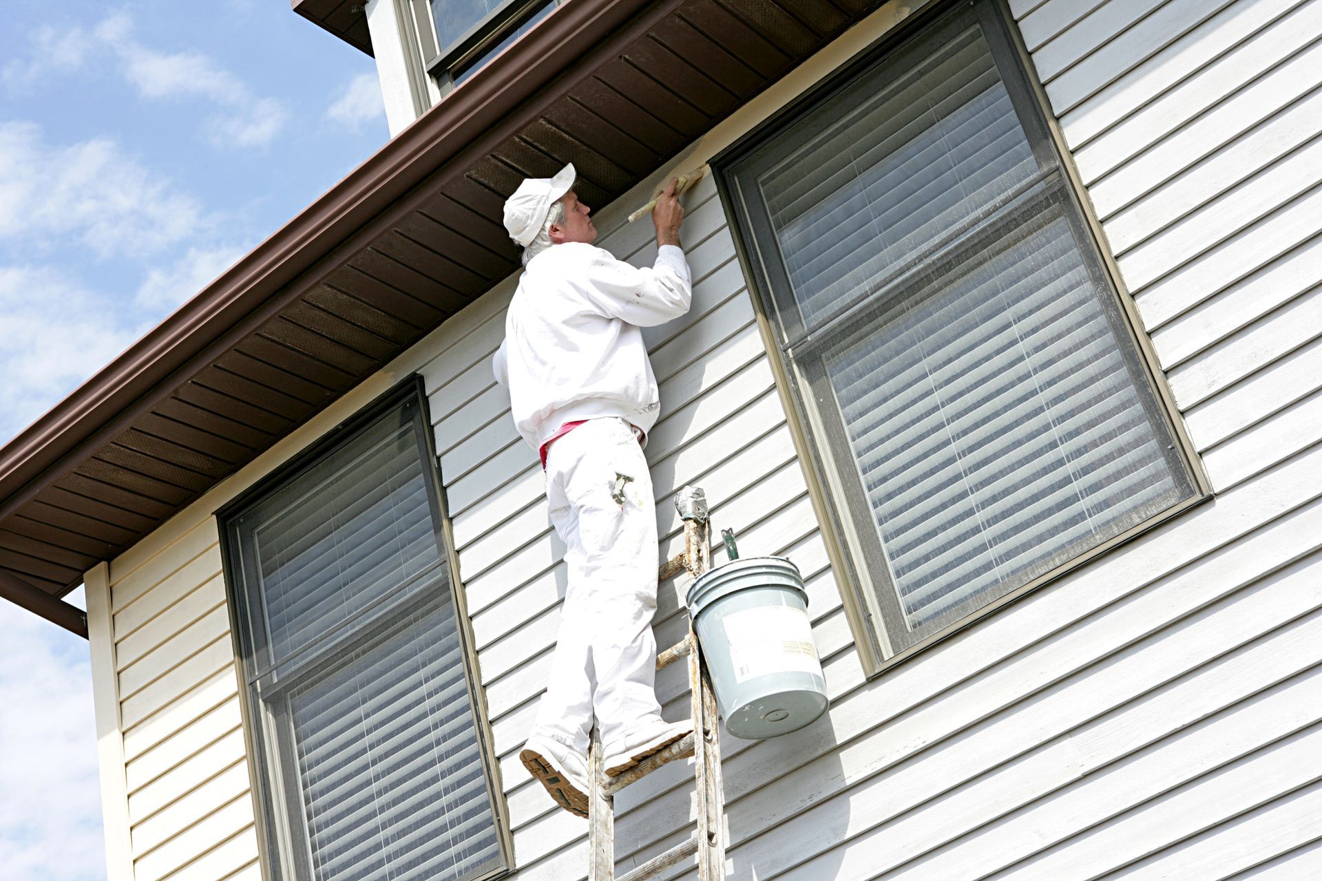 A man on a ladder is painting the side of a house
