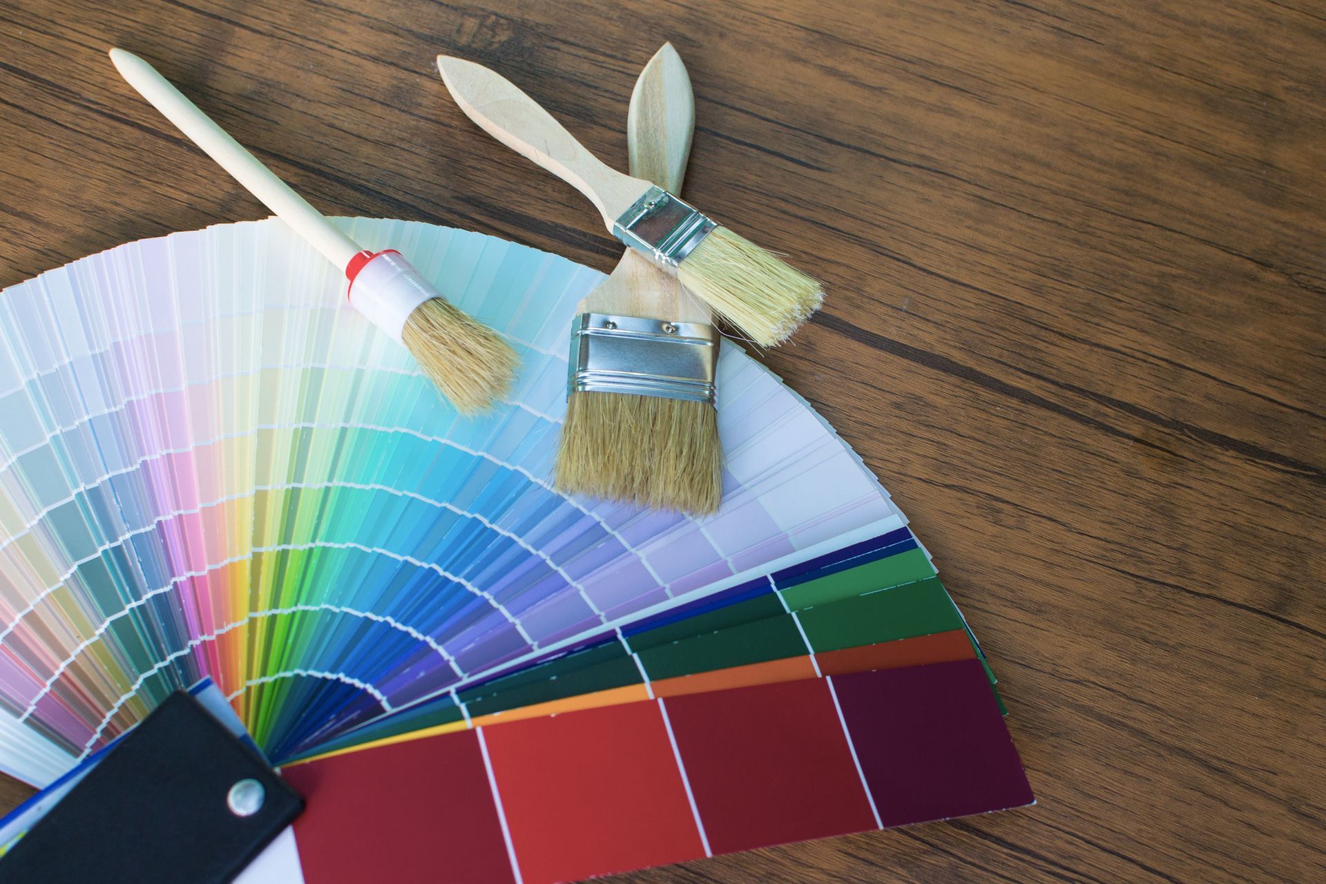 A fan of paint samples and paint brushes on a wooden table.