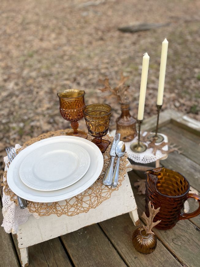 A table set for a picnic with plates , candles , cups and glasses.