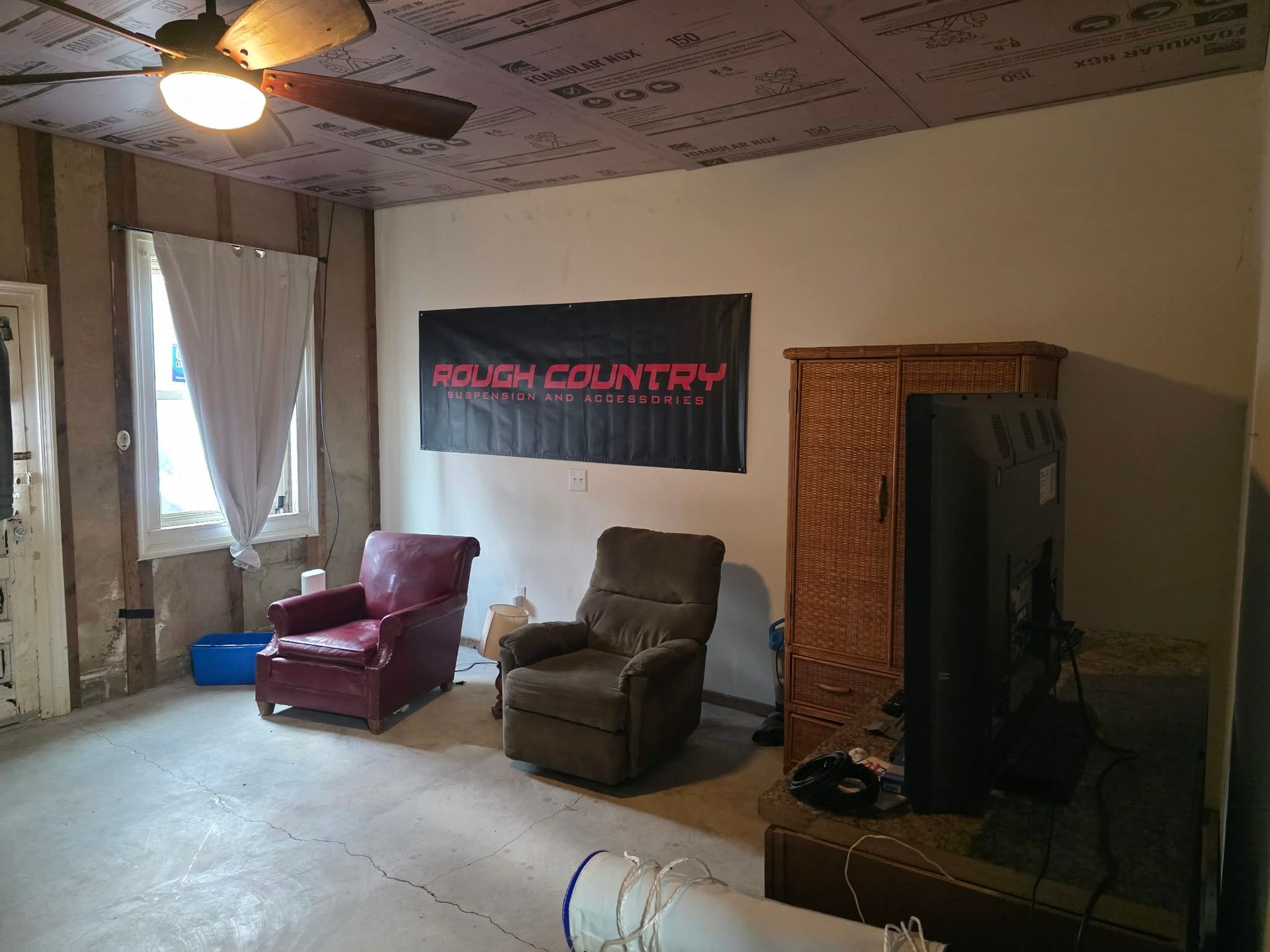 Room with chairs, a TV, and a banner for Rough Country. The ceiling is insulated, and a window is visible.