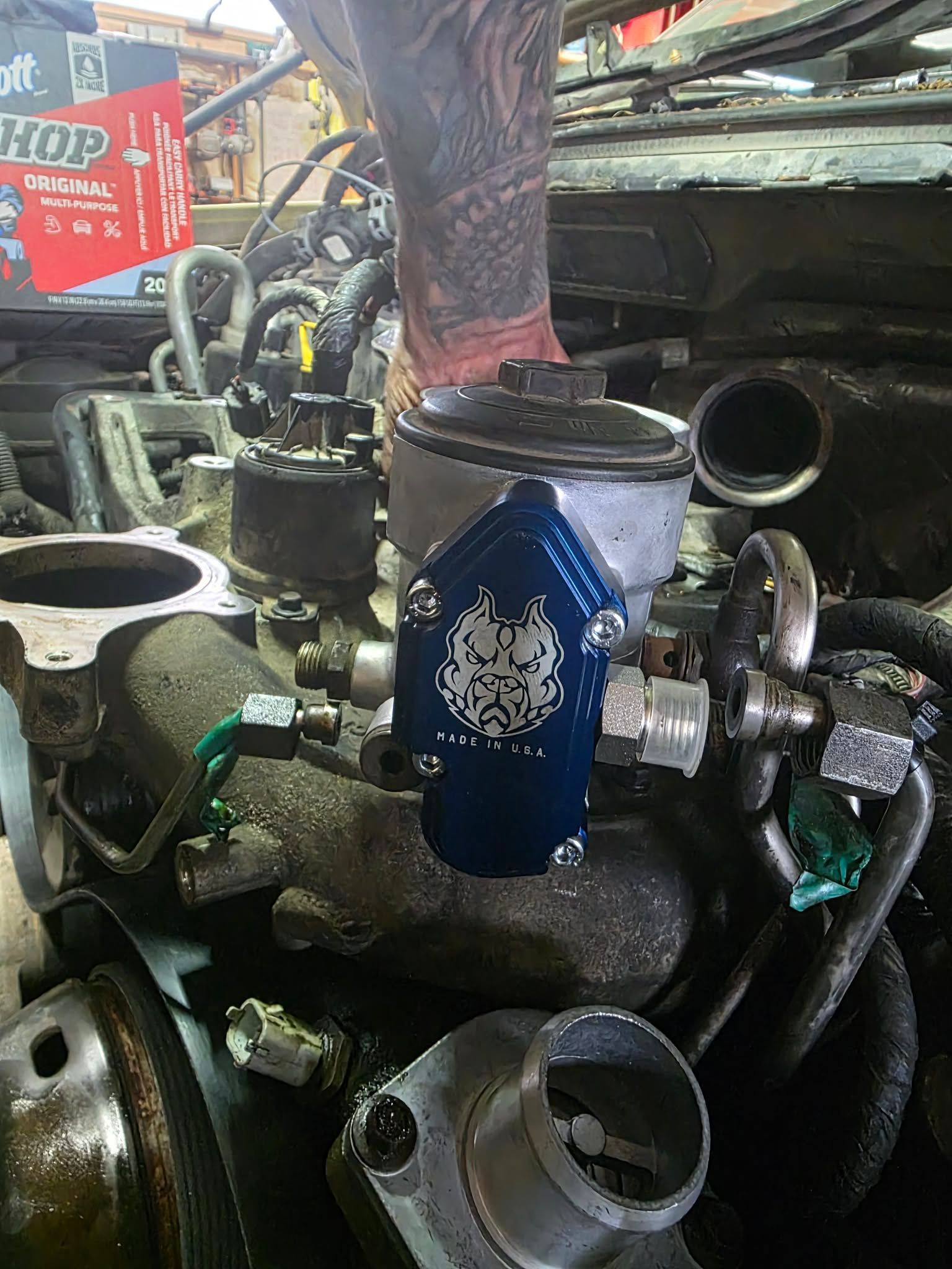 Blue automotive part installed on an engine; mechanic's tattooed arm visible. | Seth's Auto Care