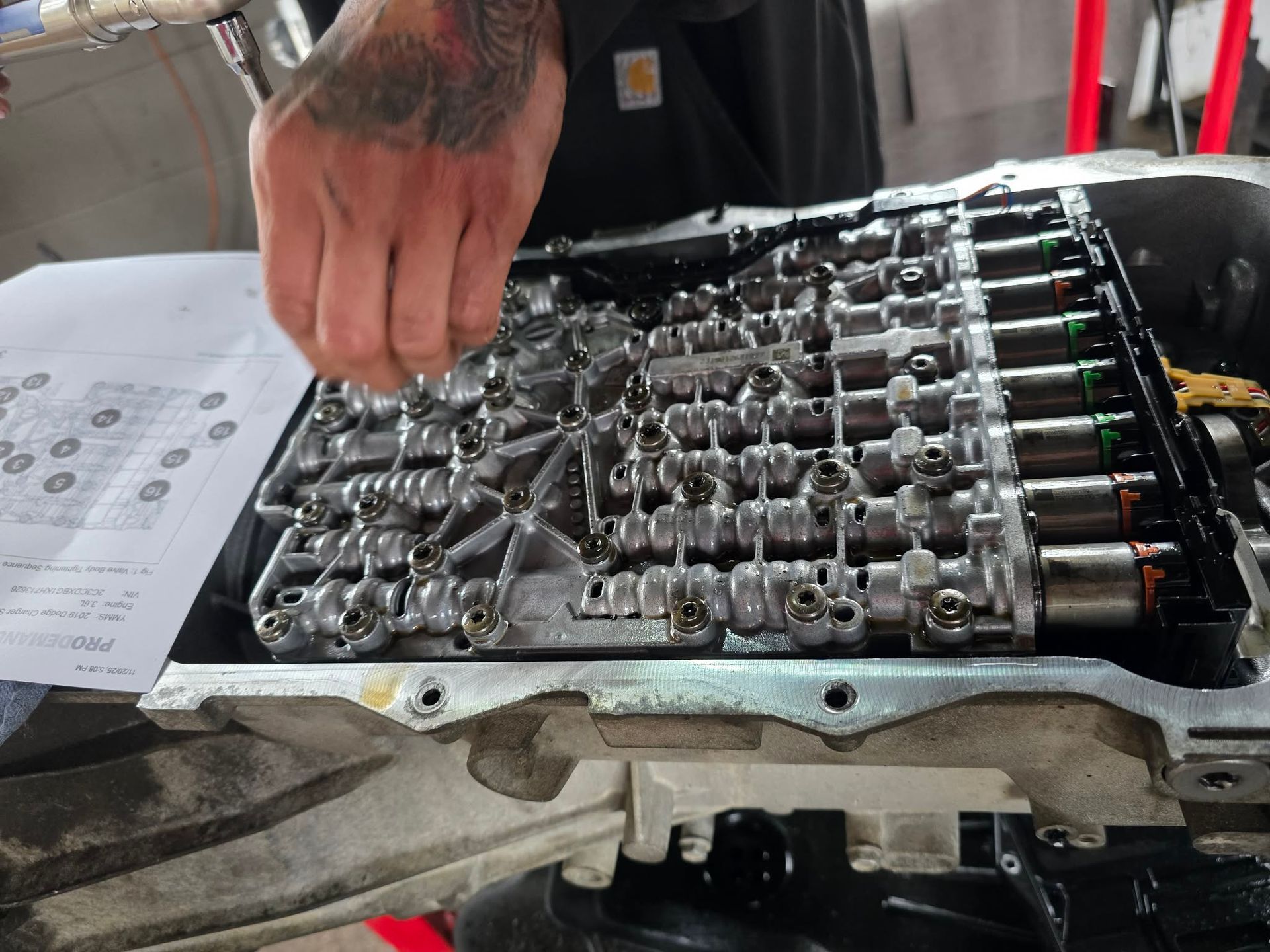 A person's hand working on an open automatic transmission valve body; tools and paper nearby. | Seth's Auto Care