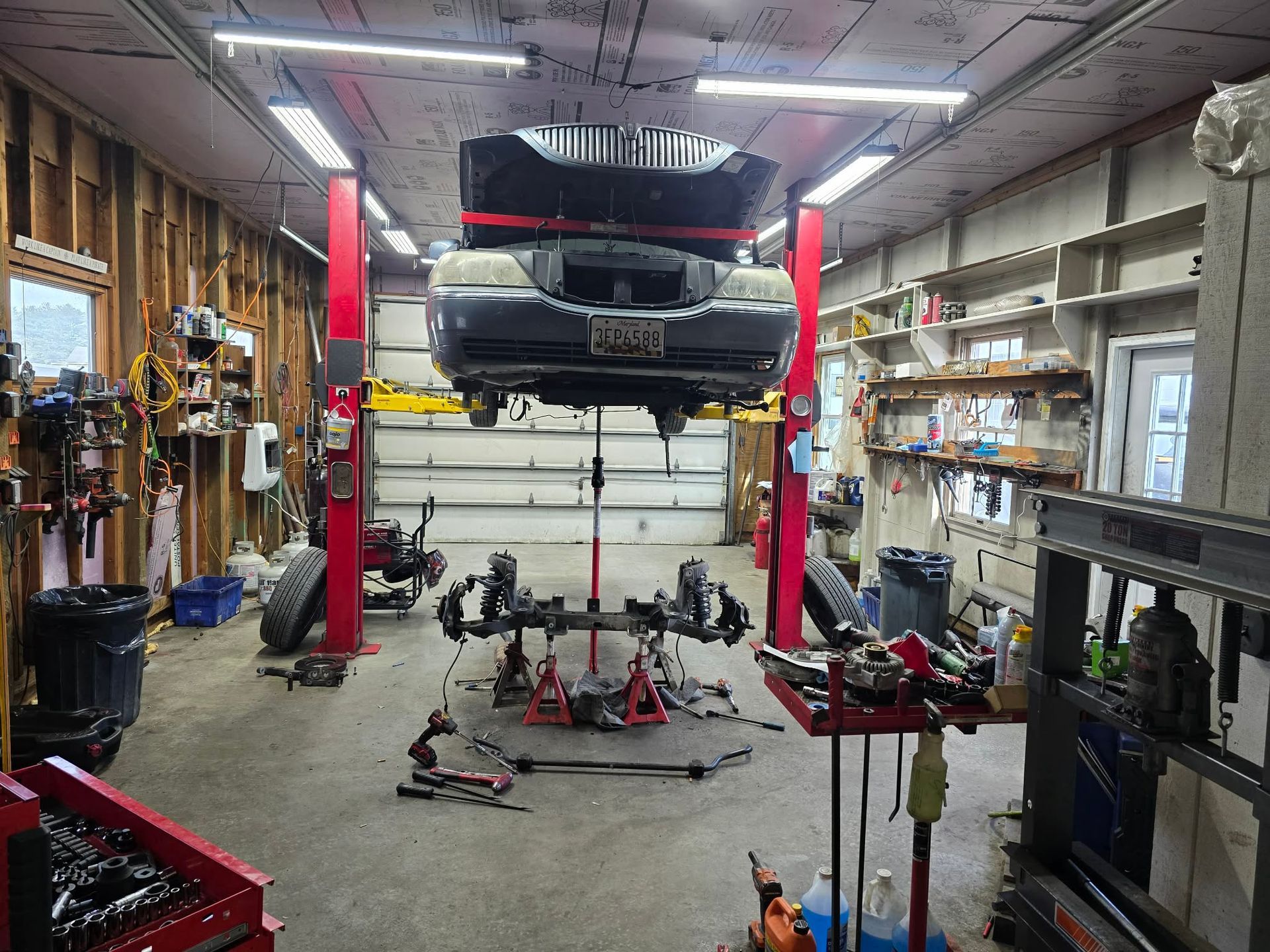 Car on a lift in a garage, suspension parts removed. Tools, shelves, and red lift posts are visible. | Seth's Auto Care