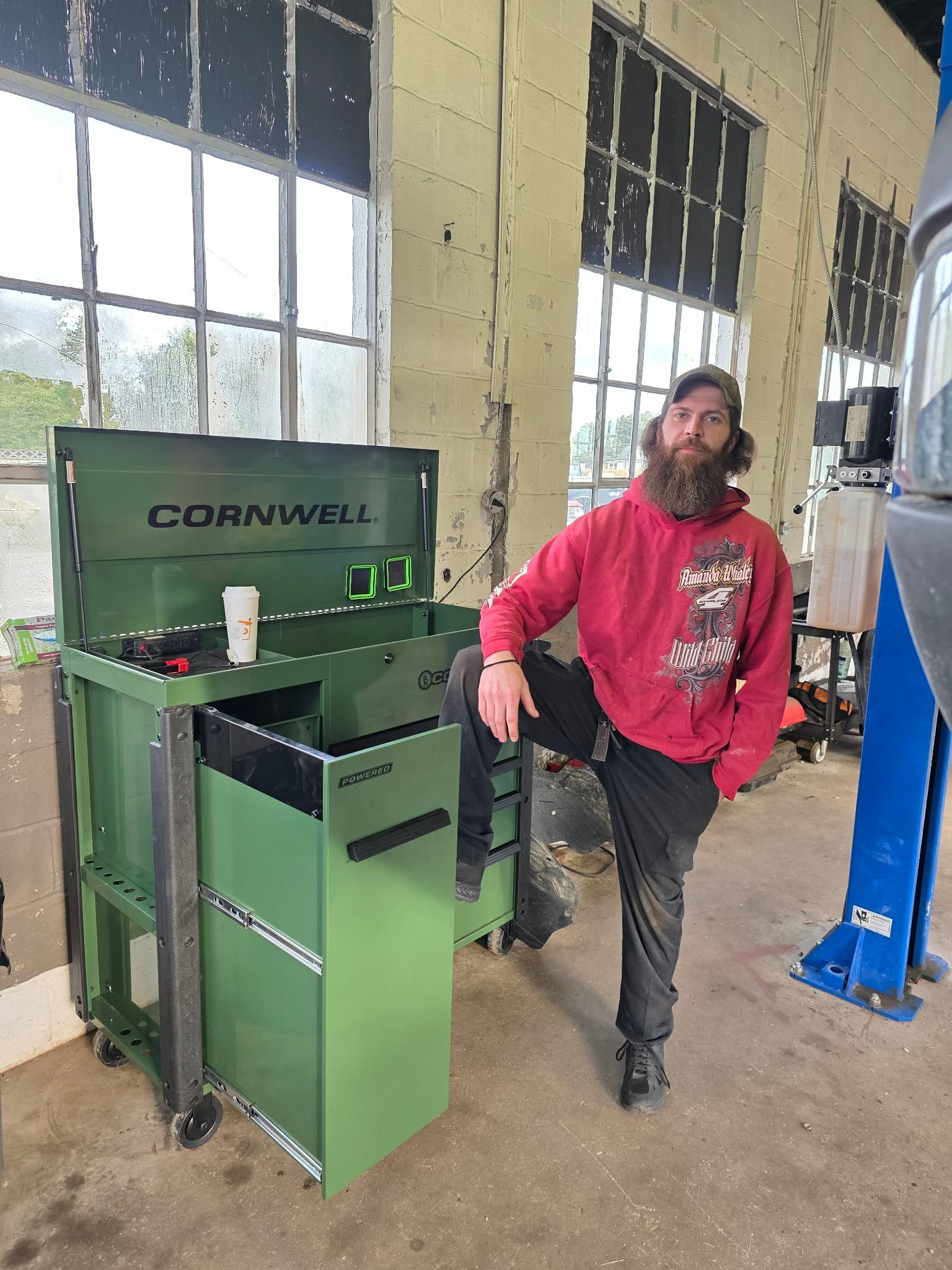 A man with a beard leans on a green Cornwell tool chest in a workshop. | Seth's Auto Care