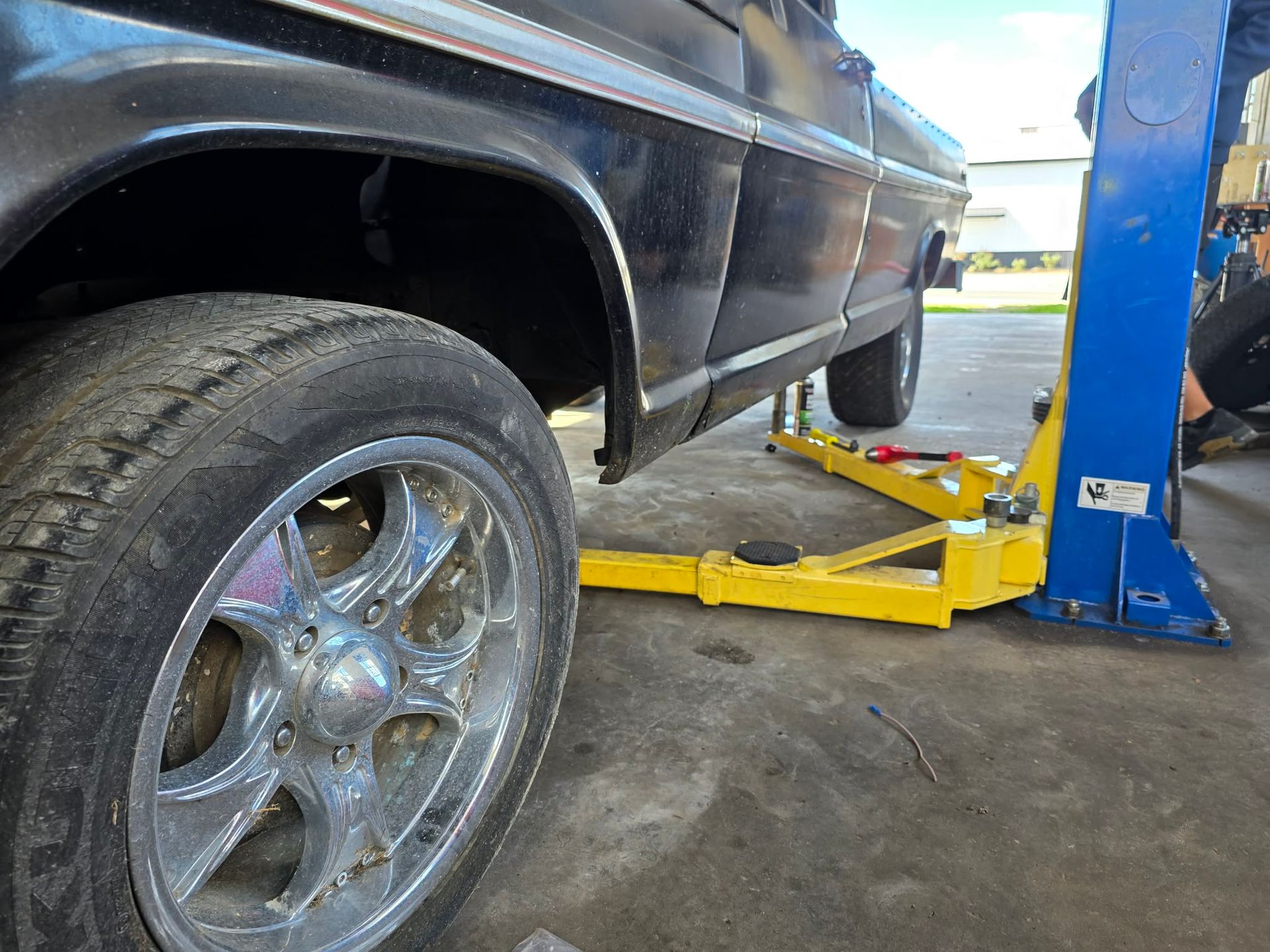 Black car raised on a yellow auto lift in a shop. Chrome wheel in focus. | Seth's Auto Care