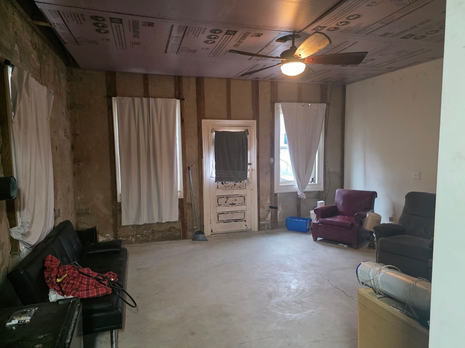 Interior room with exposed walls and ceiling, concrete floor, old door, two windows, and various furniture. | Seth's Auto Care