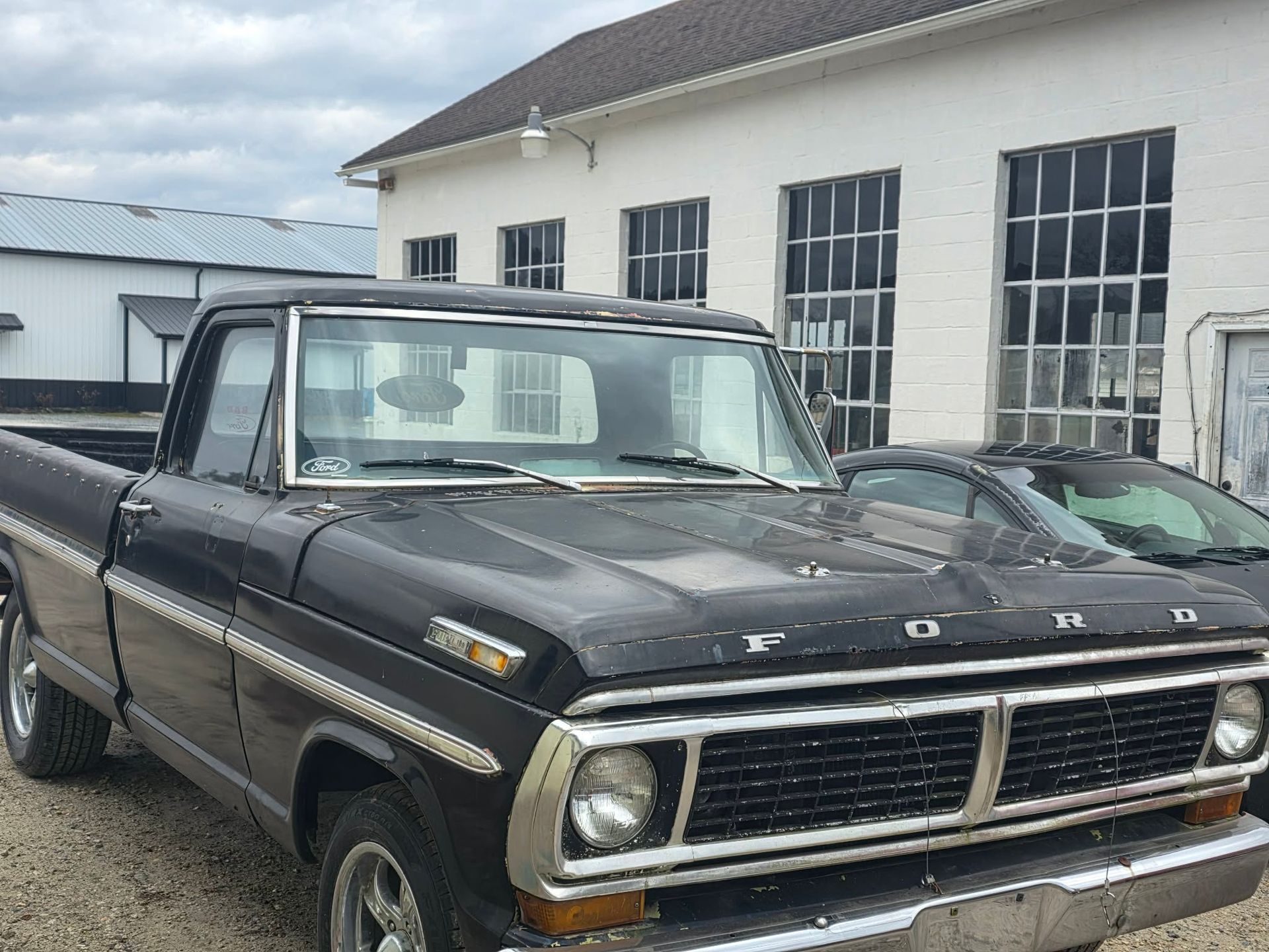 Black vintage Ford pickup truck parked outside a white building with black framed windows. | Seth's Auto Care