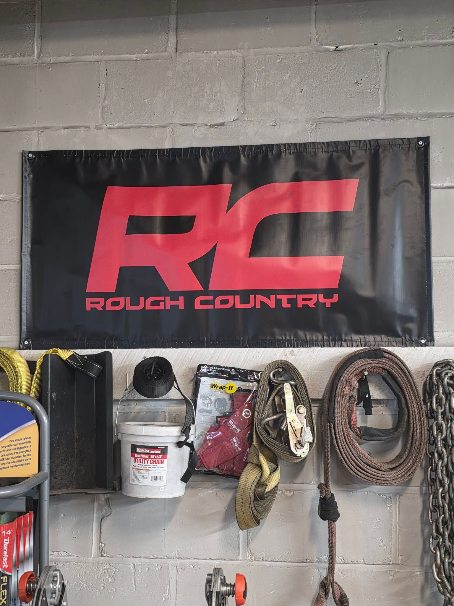 Rough Country banner on a cinder block wall, with tools and gear hanging below. Black and red. | Seth's Auto Care