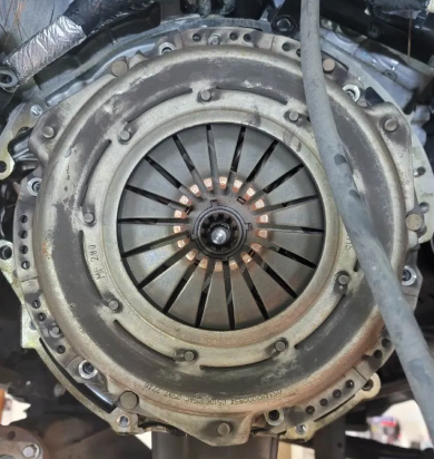 A car clutch assembly, metal and circular with numerous bolts and fins, viewed from the front. | Seth's Auto Care