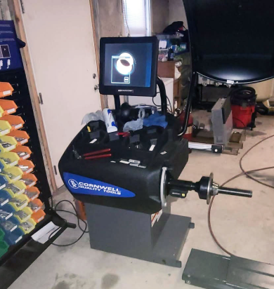 A tire balancing machine in a garage. Black and blue machine with a screen displays wheel info. | Seth's Auto Care