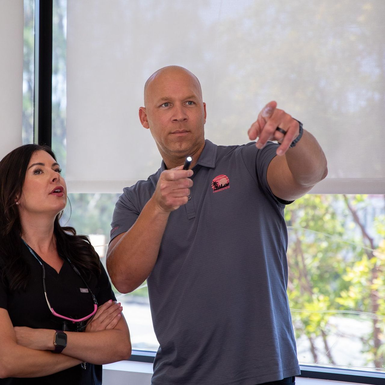 A man and a woman are standing next to each other in front of a window.