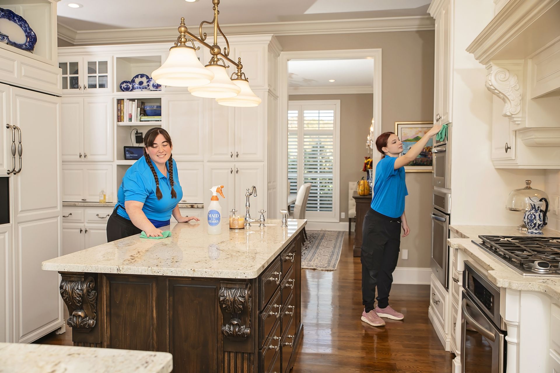 Two people cleaning a white kitchen; one wiping the island, the other wiping the wall.