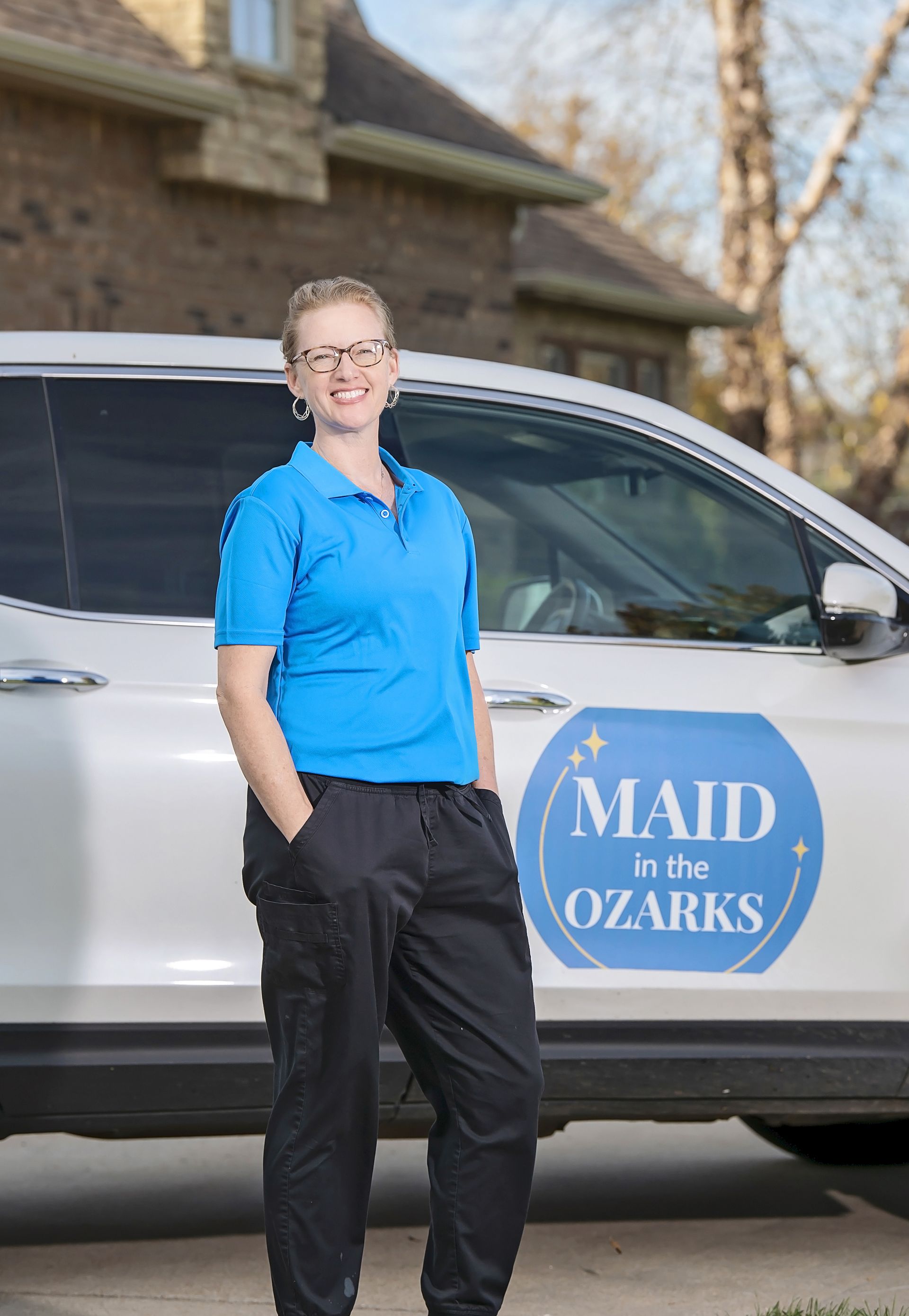 Woman dusting window blinds, green plant in sunlight.