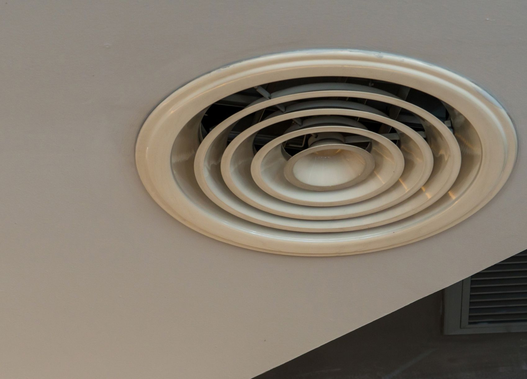 A close up of a circular air vent on a ceiling.