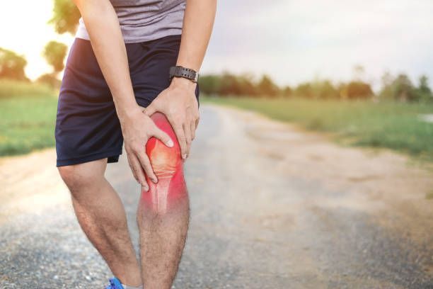 A man is holding his knee in pain while standing on a road.