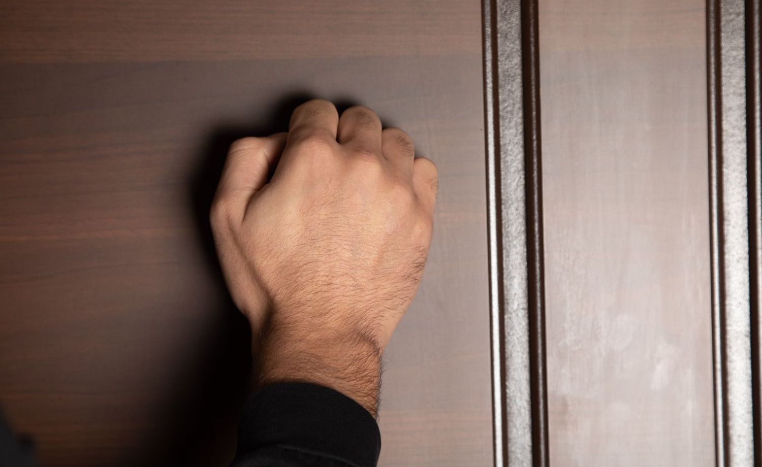 A hand knocking on a dark brown wooden door.