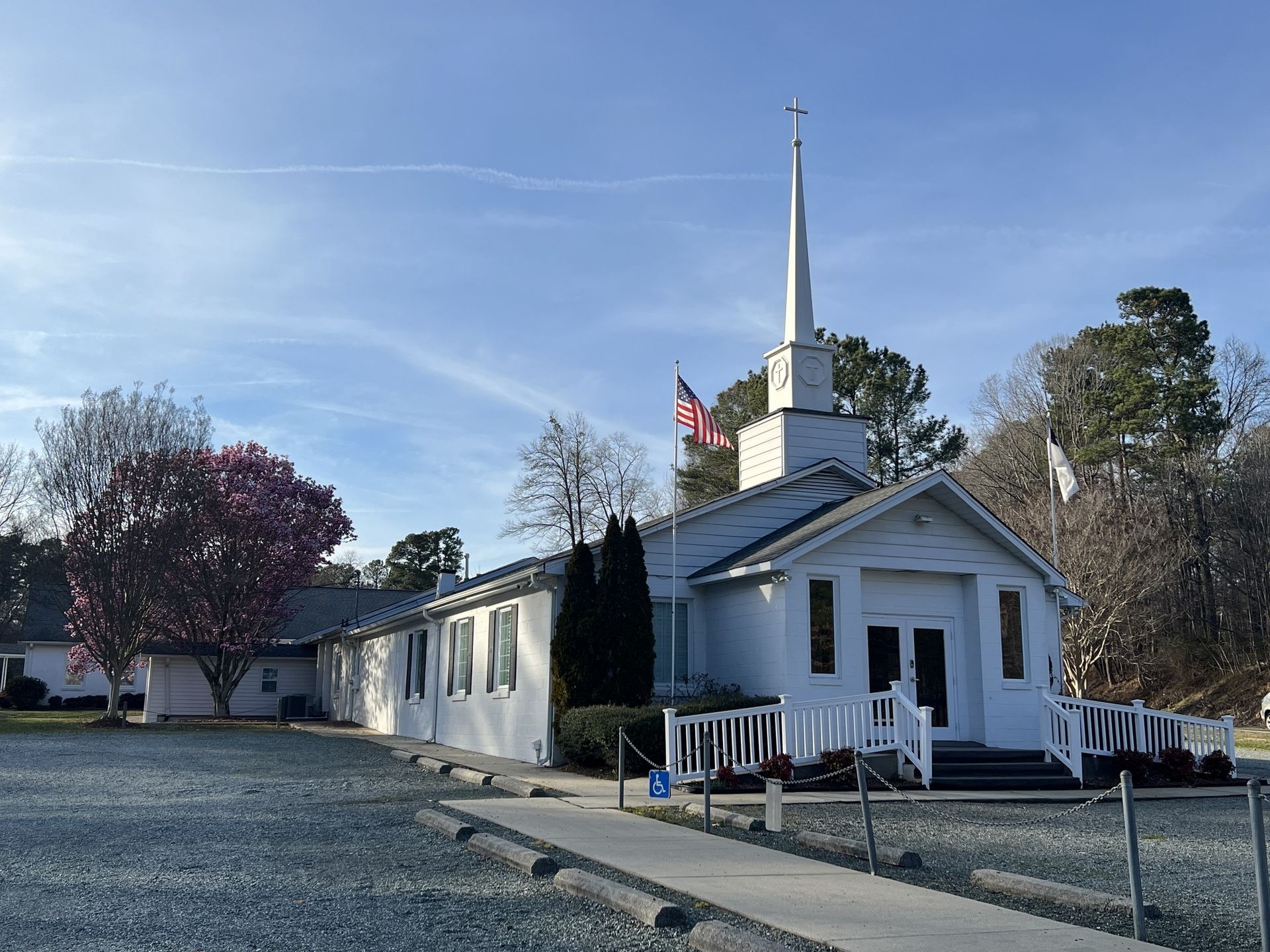 White church building with a steeple and American flag on a sunny day. A path leads to the front door.