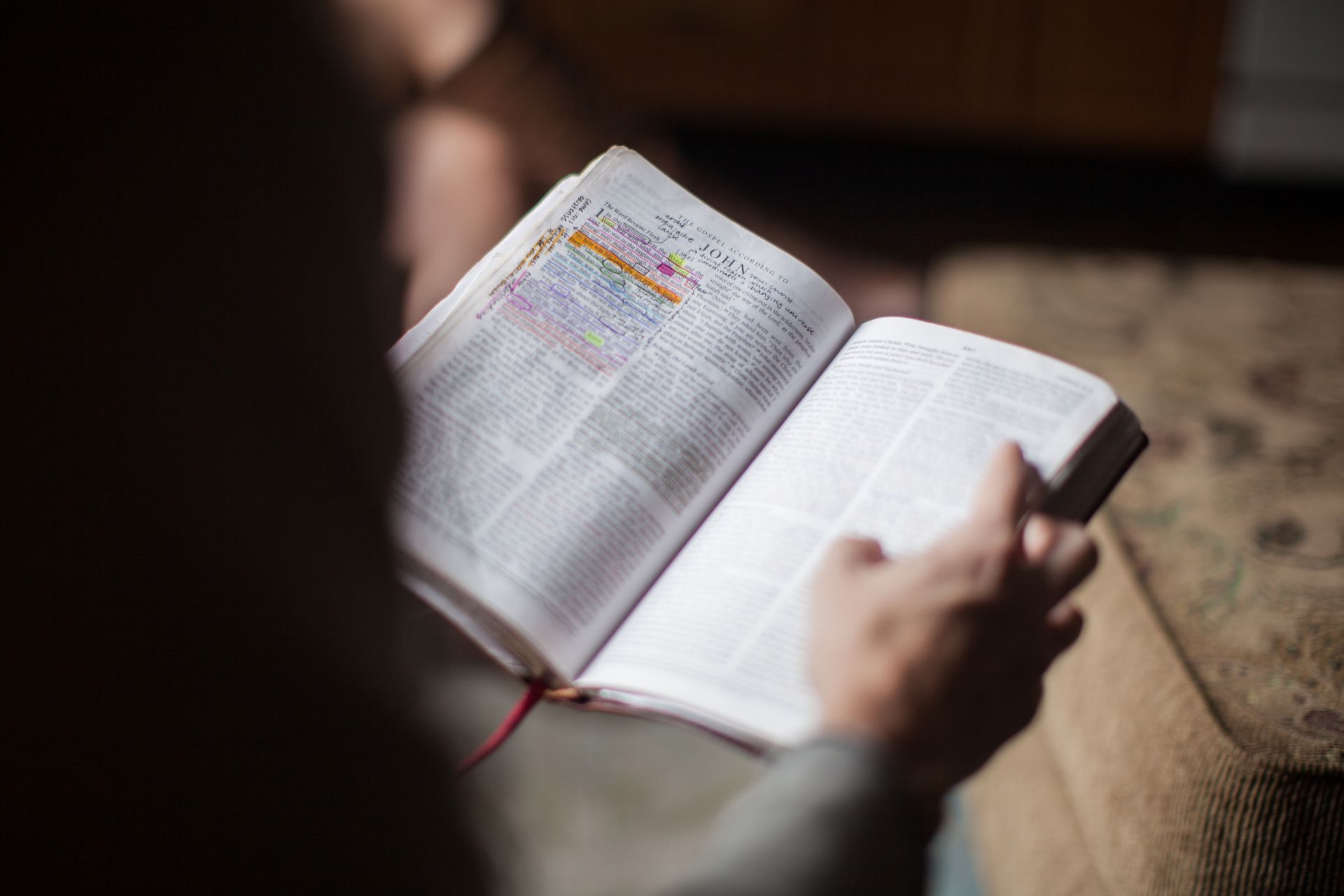 Person sitting, reading an open Bible, focusing on the text. Red ribbon bookmark.