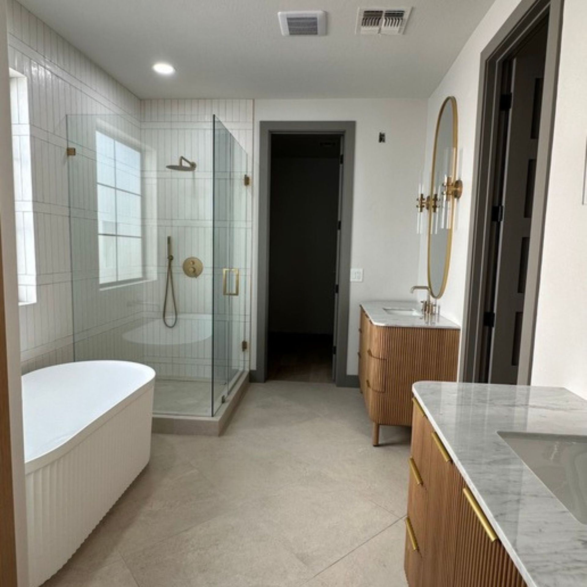 Modern bathroom with a white bathtub, glass shower, and light wood vanities.