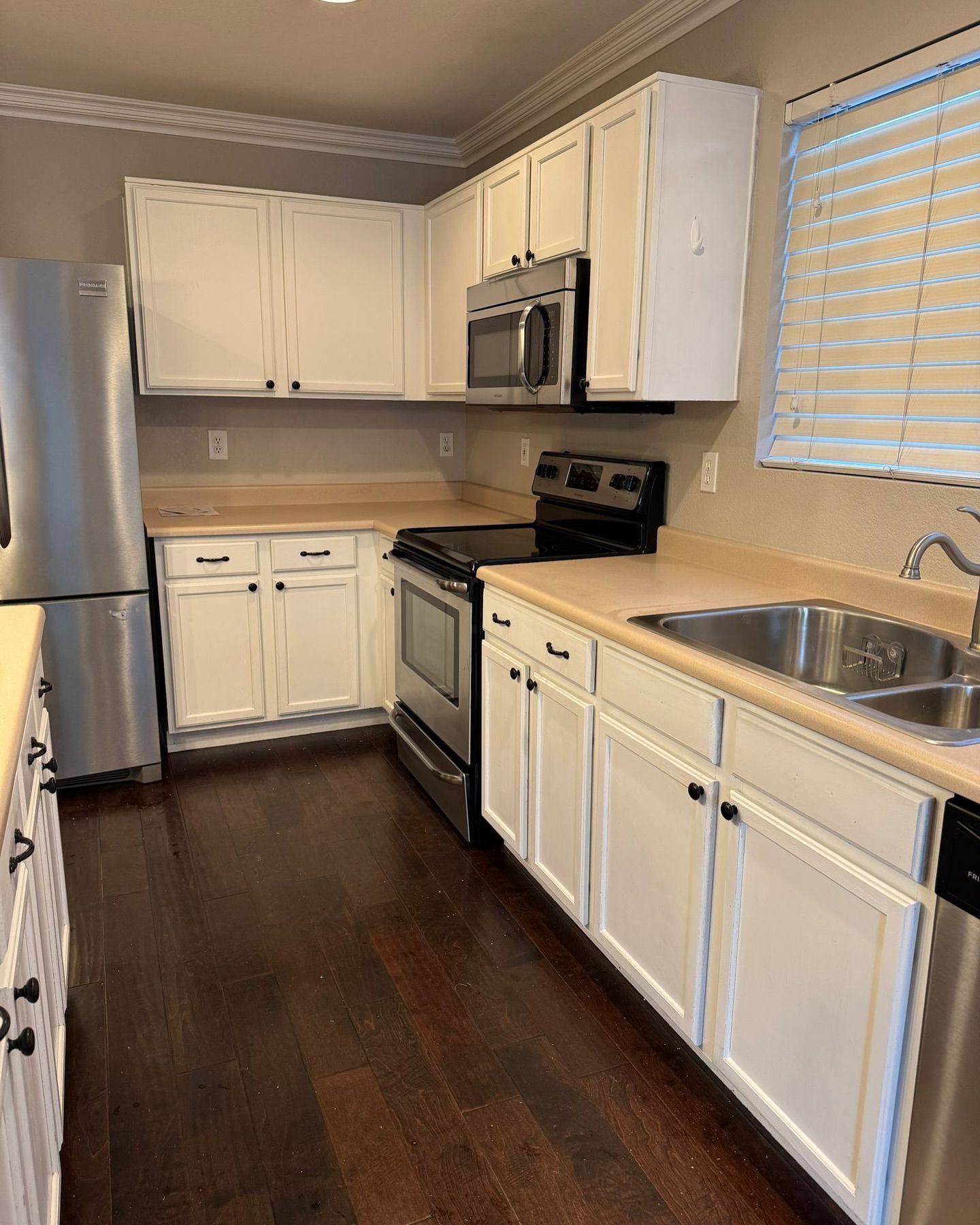 A kitchen with white cabinets , stainless steel appliances , a sink and a refrigerator.