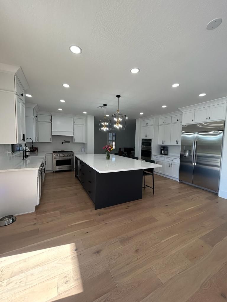 A kitchen with white cabinets and stainless steel appliances and a large island in the middle.