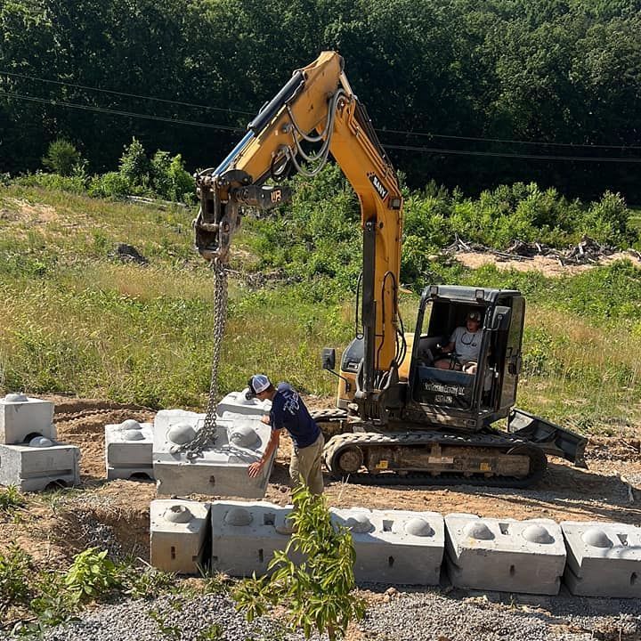 A man is standing next to a yellow excavator in a field.