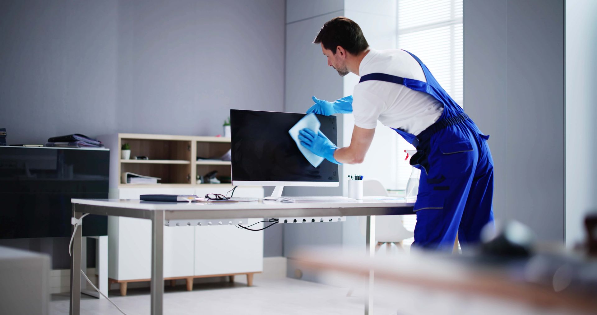 A man is cleaning a computer screen in an office.