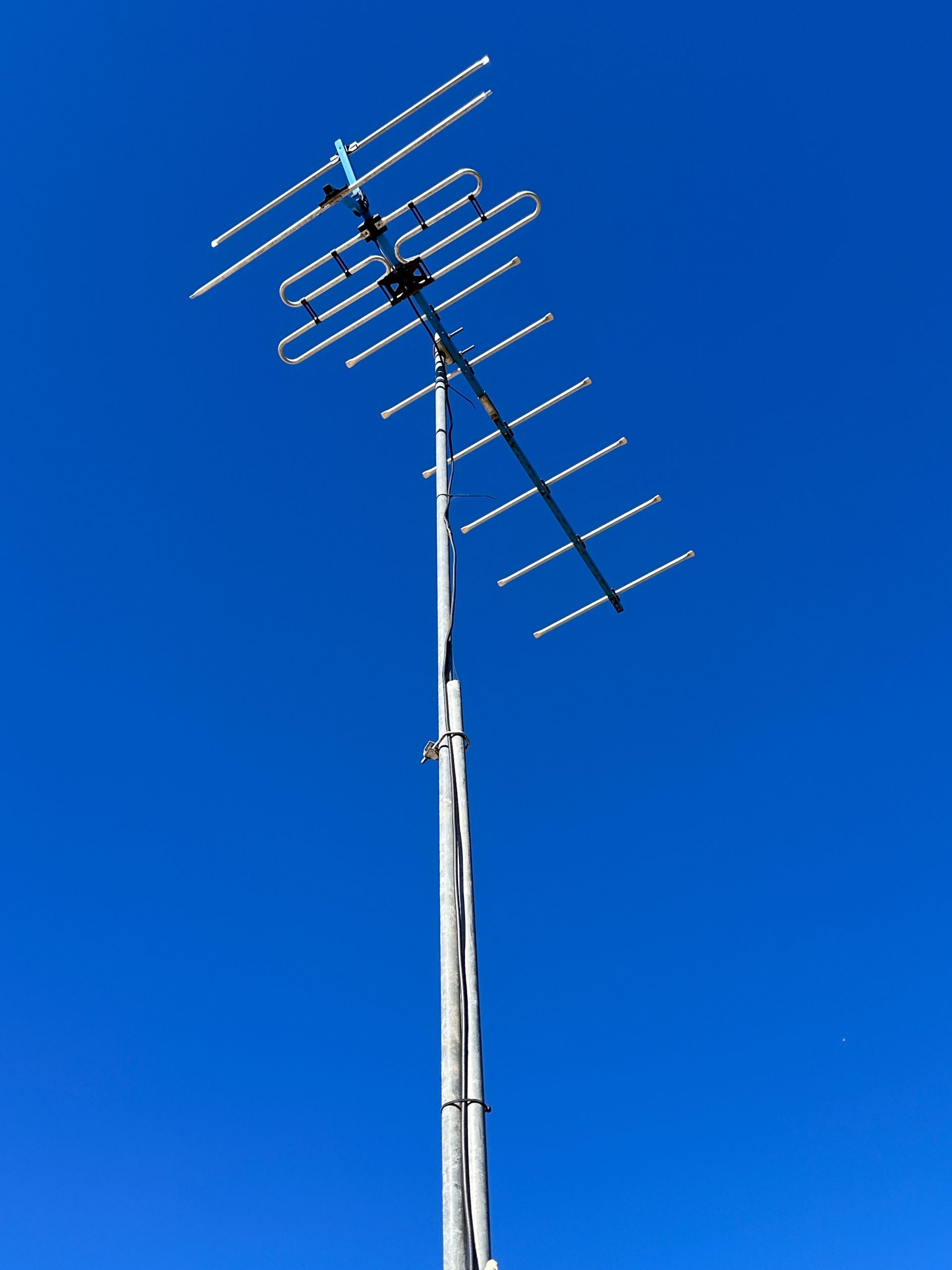 A person in a rust-colored sweater smiling while looking at a yellow smartphone, sitting on a couch in a bright room.