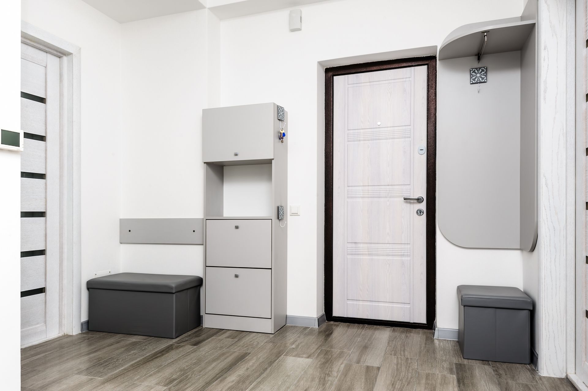 A hallway with a door , a bench , a shoe rack , and a coat rack.