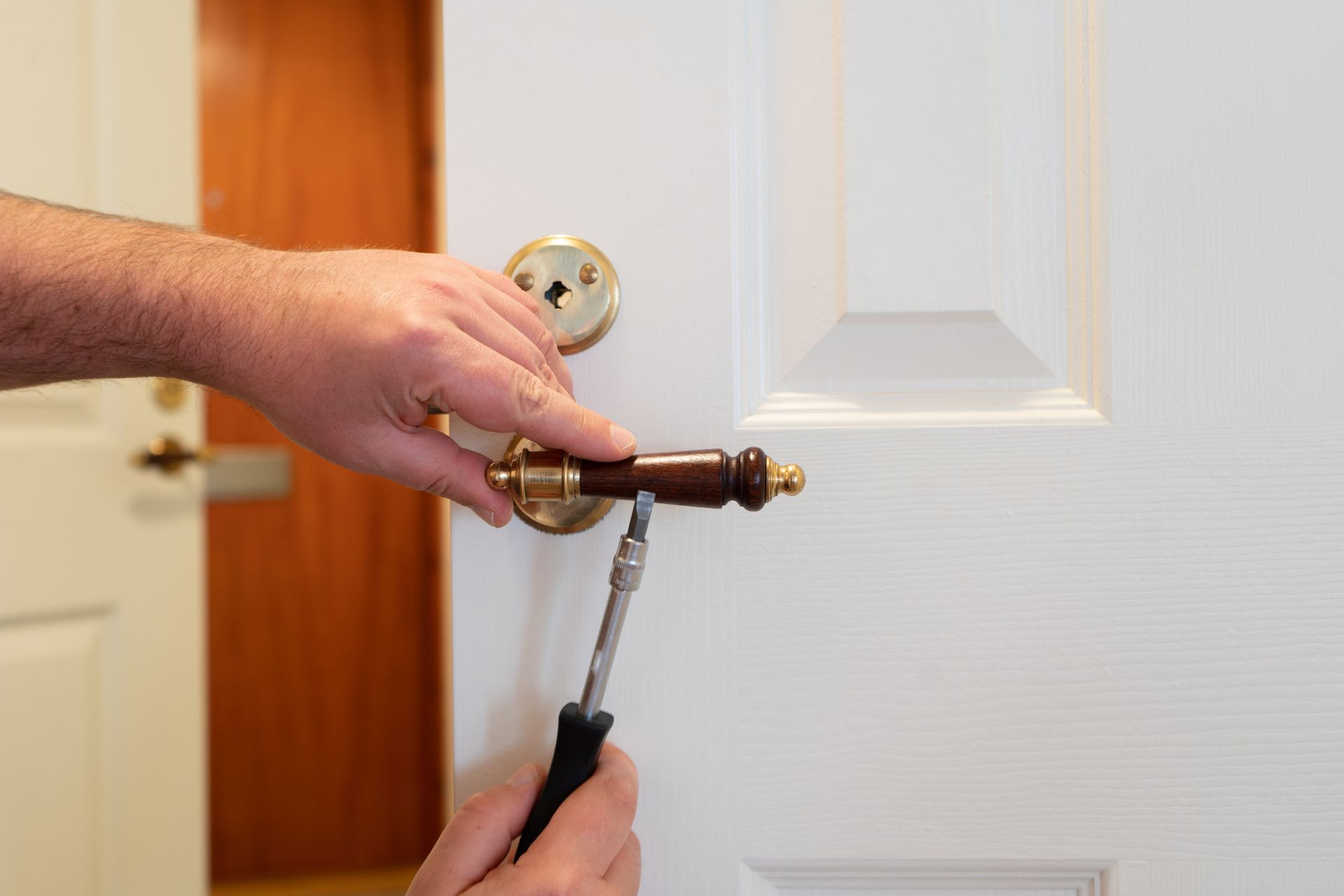 A person is fixing a door handle with a screwdriver.