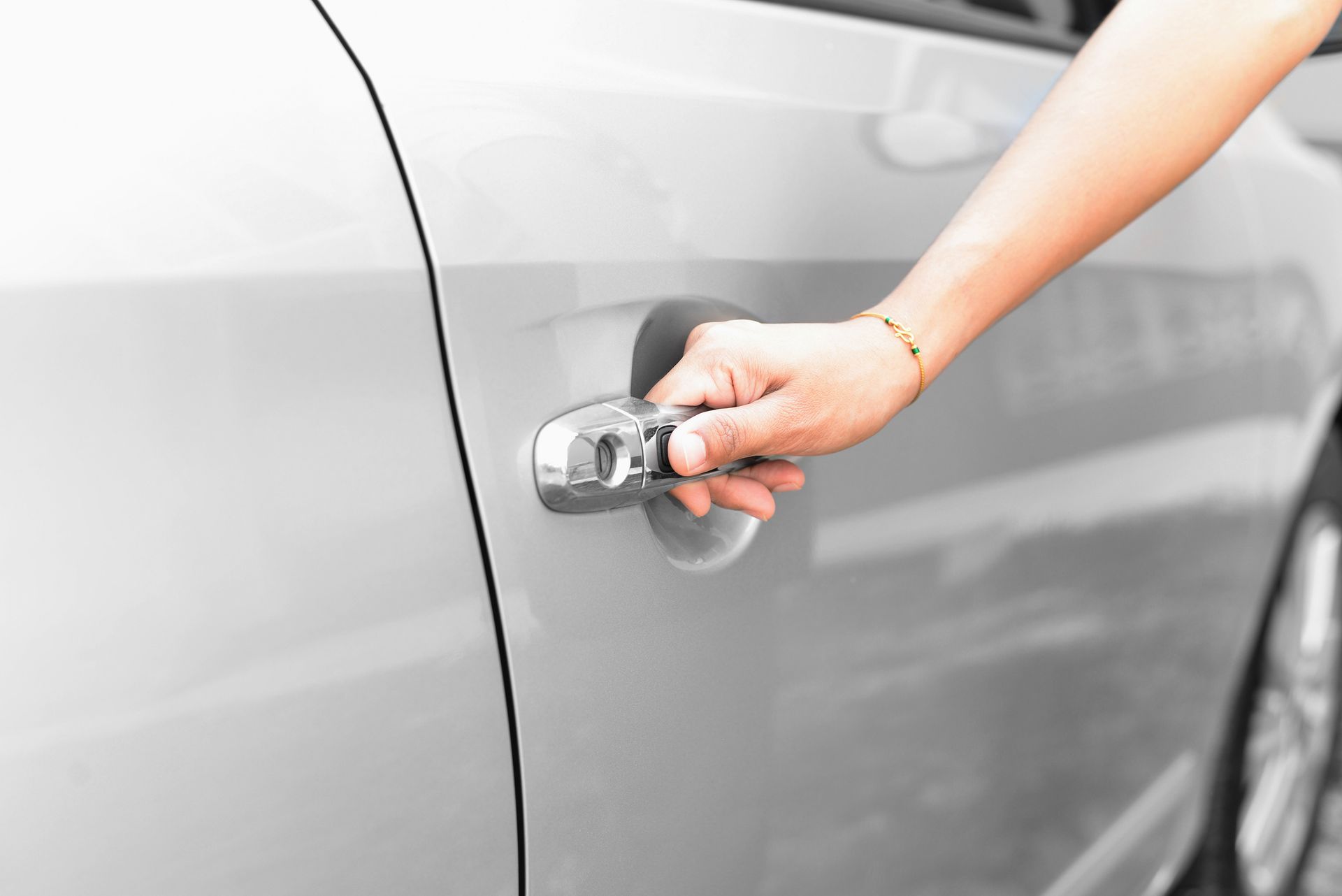 A person is opening the door of a silver car.
