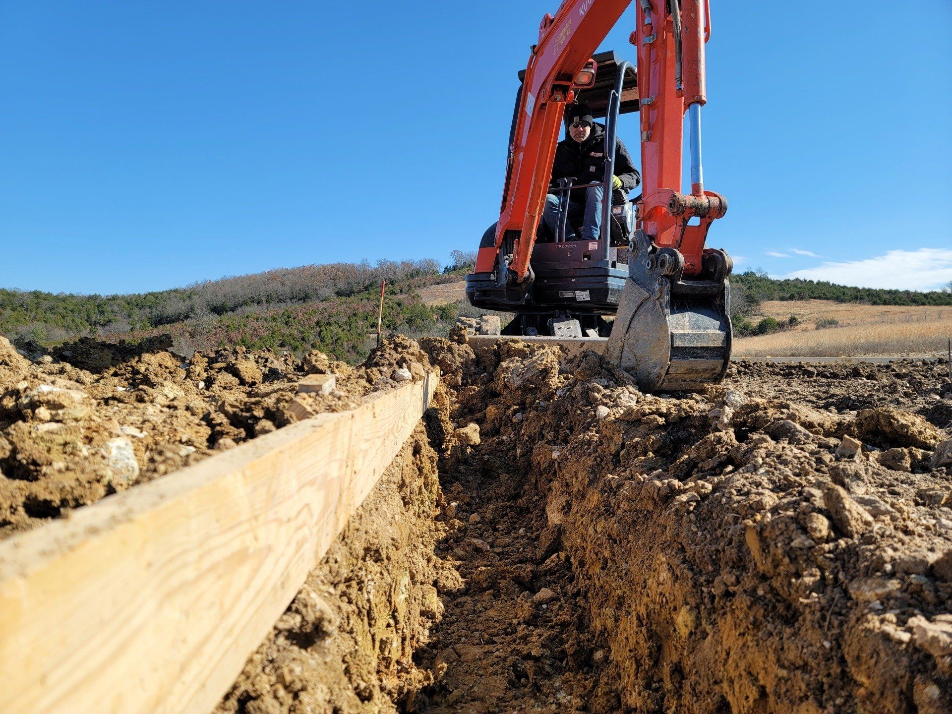 A man is driving an excavator in a dirt field.
