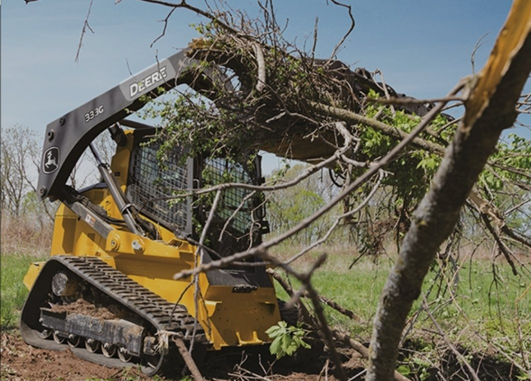 skid steer grabbing brush with it's front end and lifting it out. rough cuts construction.