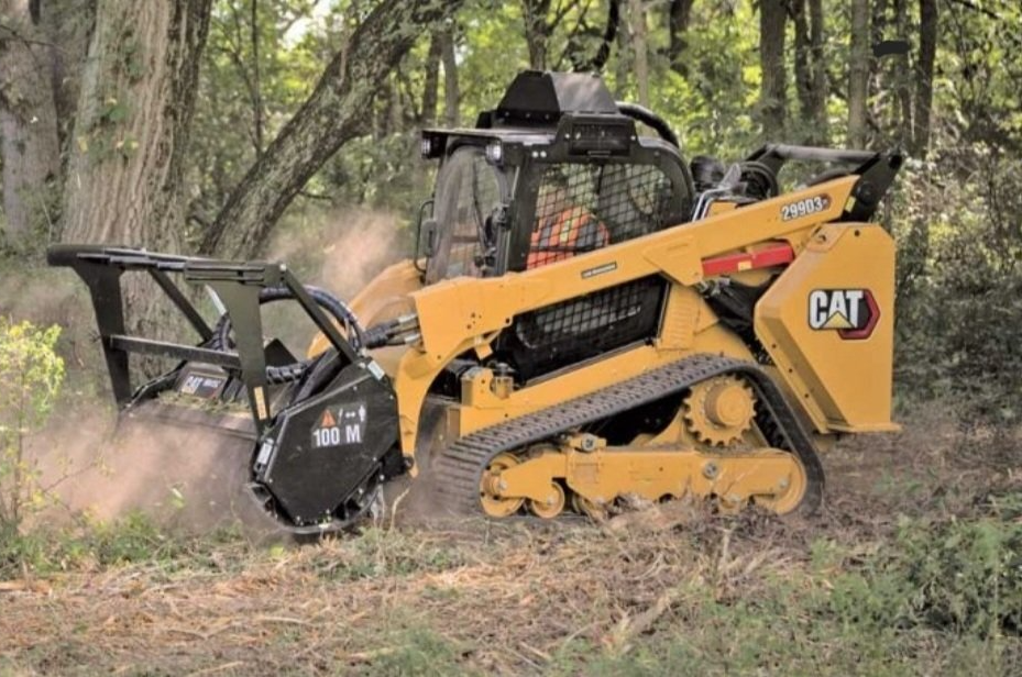 A cat tractor is cutting trees in the woods