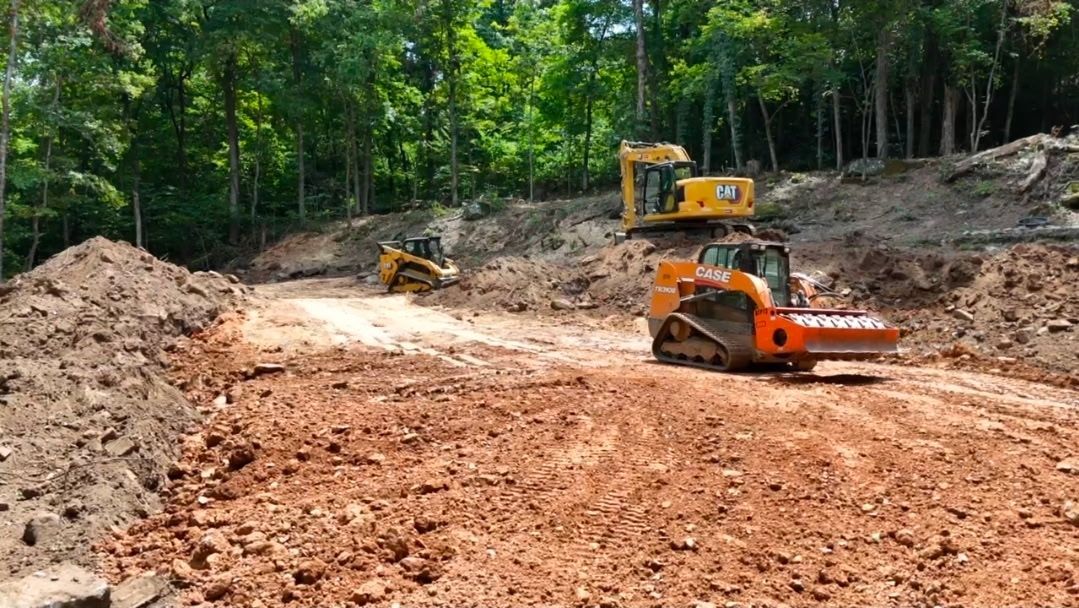 Rough Cuts Construction worker operating a backhoe dumping dirt gathered from a trench being dug.